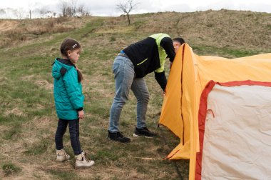 Bereketli yeşil bir çayırda, bir baba canlı turuncu bir çadır kurmaya odaklanırken, genç kızı da kamp deneyimine katılmak için can atıyor..