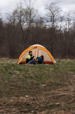 Dostlar parlak turuncu bir çadırın içinde rahatça oturup sohbet ederken serin bir esinti yakınlardaki ağaçların arasında hışırdıyor, açık havada geçirdikleri zamanın tadını çıkarıyorlar..