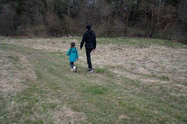 Bir çocuk, ağaçlar ve yumuşak otlarla çevrili, dolambaçlı bir yolda, bir yetişkinin yanında neşeli bir şekilde koşar. Sıcak ve macera dolu huzurlu bir atmosfer yaratır..
