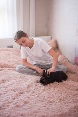 Genç bir kadın lüks pembe bir yatakta oturur, küçük siyah bir tavşanı severek okşar. Sahne sakin ve samimi, insan ve hayvan arasındaki hassas bağlantıyı gösteriyor..