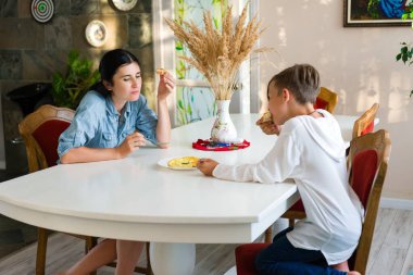 Bir anne ve oğlu beyaz bir masada oturup yemek yiyorlar. Güneş ışığı odaya akıyor, sahneyi aydınlatıyor. Birlikte rahat bir anın tadını çıkarıyorlar..