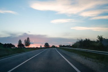 Bereketli yeşilliklerle çevrili dolambaçlı bir yol boyunca huzurlu bir sürüş. Güneş batarken, uzak bir köyde, gün batımından hemen sonra gökyüzünde canlı renkler bırakarak..