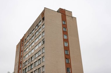 Yüksek katlı bir bina, iç karartıcı bulutlu bir gökyüzüne doğru uzanan ve kentsel bir manzaranın yalnızlığını kapsayan soyulmuş boyaları ve çıplak pencereleri gözler önüne seriyor..