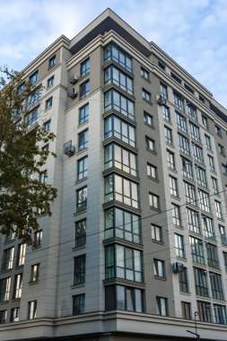 Çağdaş bir şehir binasının cam pencerelerinden yansıyan güneş ışığı, zarif tasarımını ve modern özelliklerini vurgularken aşağıdaki yemyeşil çimenlik tarafından çerçeveleniyor..