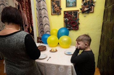 Bir yetişkin güzel dekore edilmiş bir doğum günü pastasını açmaya hazırlanırken bir çocuk şenlik masasında gözlerini kapar ve saf mutluluğu yakalar..