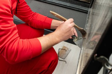 Kapalı alan ortamında, canlı kırmızı bir kıyafet giymiş odaklanmış bir birey etraflarındaki odanın estetiğini geliştirmek için bir fırçayla dikkatlice boya sürer..