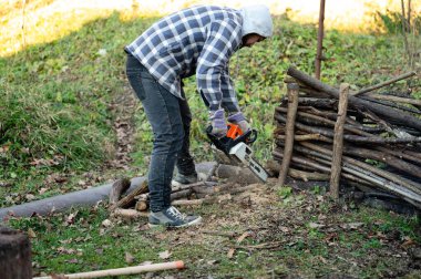 İşine odaklanmış bir marangoz, gür bir ormanda kütük kesmek için elektrikli testere kullanır..