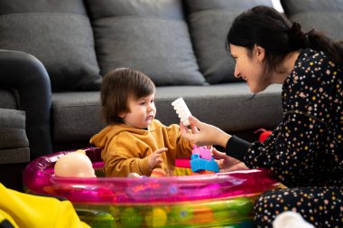 Bir bakıcı ve küçük bir çocuk birlikte oynarken neşeli bir etkileşim başlar. Canlı şişme havuz renkli oyuncaklarla dolu. Hoş bir ortam yaratıyor..