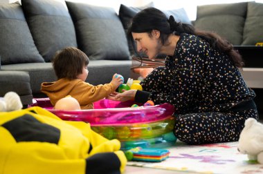 Sıcak bir yuva ortamında, sevgi dolu bir anne ve küçük çocuğu neşeyle birlikte oynuyorlar..