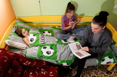 Üç arkadaş neşeli bir odada toplanıp renkli bir yatak örtüsünde hikayelerini paylaşıyorlar. Biri okurken, diğeri telefonda arkadaşlıkla dolu sıcak bir atmosfer yaratıyor..