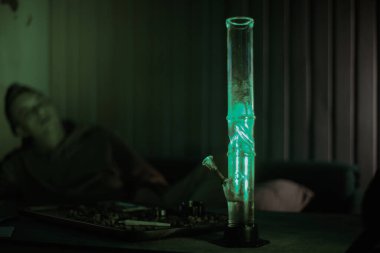 Bir adam uyur, bir nargilenin arka planına yaslanır ve esrarlı bir masaya uzanır. Sakinleşmek ve uyumak için ot. ilaç