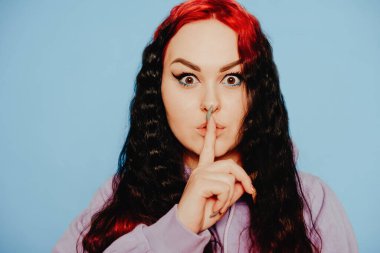 Mavi arka planda mavi kazaklı bir kadın poz veriyor. Uzun saçlı ve kulaklarında tüneller olan güzel bir esmer. Göz kalemi ve moda makyaj