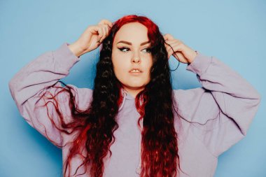 Mavi arka planda mavi kazaklı bir kadın poz veriyor. Uzun saçlı ve kulaklarında tüneller olan güzel bir esmer. Göz kalemi ve moda makyaj