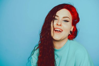 Mavi arka planda mavi kazaklı bir kadın poz veriyor. Uzun saçlı ve kulaklarında tüneller olan güzel bir esmer. Göz kalemi ve moda makyaj