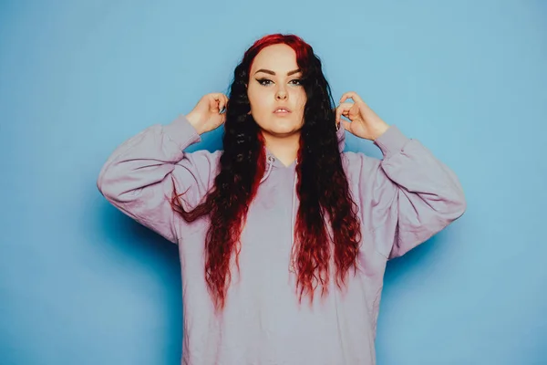 stock image Woman in a blue sweater on a blue background posing. A beautiful brunette with long hair and and tunnels in her ears. Eyeliner and trendy makeup