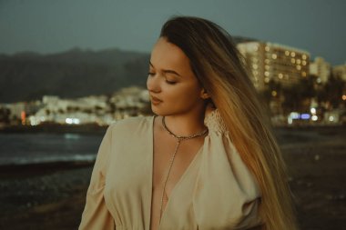 Gorgeous girl in a dress and jewelry on the background of the sunset on the background of the sea, a woman with long hair on vacation portrait, palm trees