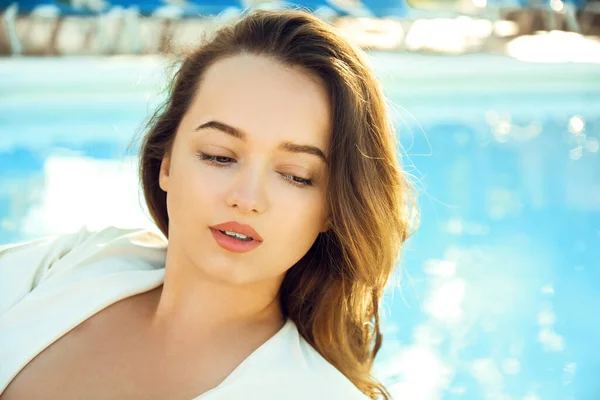 Beautiful girl portrait on the background of the pool and water, natural makeup, beautiful hair and clean skin, sun creams.
