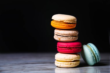 Macaron pink, orange and beige, blue on marble style and black background. French dessert on top of each other