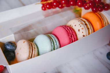 Macaron dessert, a box with colorful macarons lies on a marble style. Sweets, diet, gift for March 8 or February 14. Strawberries and lingonberries, blueberries