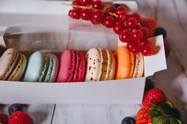Macaron dessert, a box with colorful macarons lies on a marble style. Sweets, diet, gift for March 8 or February 14. Strawberries and lingonberries, blueberries