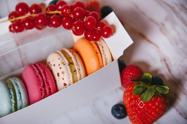 Macaron dessert, a box with colorful macarons lies on a marble style. Sweets, diet, gift for March 8 or February 14. Strawberries and lingonberries, blueberries