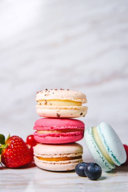 Macaron pink, orange and beige, blue on marble style. A beautiful and beautiful French dessert. Fruits, Strawberries and lingonberries, blueberries, raspberries