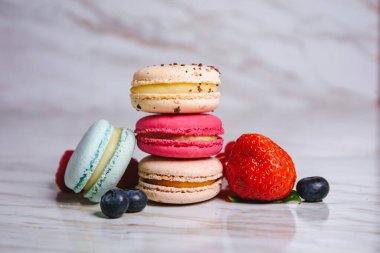Macaron pink, orange and beige, blue on marble style. A beautiful and beautiful French dessert. Fruits, Strawberries and lingonberries, blueberries, raspberries