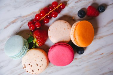 Macaron pink, orange and beige, blue on marble style. A beautiful and beautiful French dessert. Fruits, Strawberries and lingonberries, blueberries, raspberries