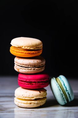 Macaron pink, orange and beige, blue on marble style and black background. French dessert on top of each other