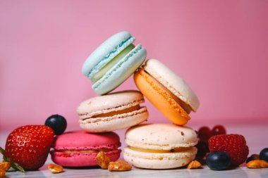 Colorful macarons. Small French cakes. Sweet and colorful french macaroons. Many tasty macarons with fresh berries, raspberries and blueberries, nuts and strawberries on a pink background