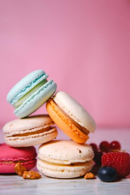 Colorful macarons. Small French cakes. Sweet and colorful french macaroons. Many tasty macarons with fresh berries, raspberries and blueberries, nuts and strawberries on a pink background