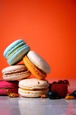 Colorful macarons. Small French cakes. Sweet and colorful french macaroons. Many tasty macarons with fresh berries, raspberries and blueberries, nuts and strawberries on a red background