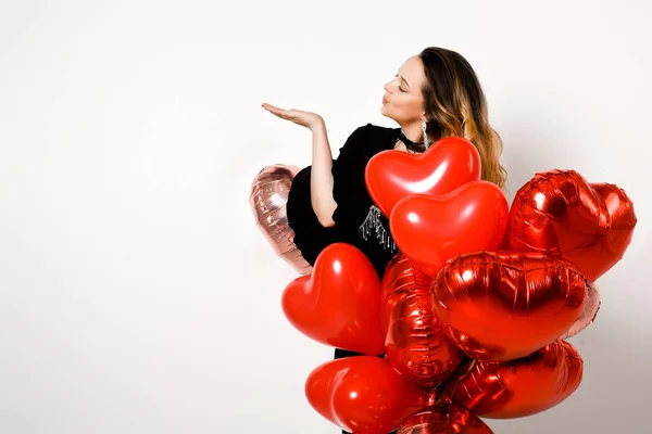 Cute woman in a black dress and corset, in jewelry and raincoats with red balloons on a white background. Fashion and fashion, valentine\'s day, air kiss, place for text or product