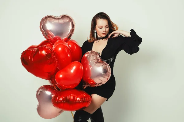 Gorgeous girl in a black dress and corset, in jewelry and raincoats with red balloons on a white background. Fashion and fashion, Valentine\'s Day