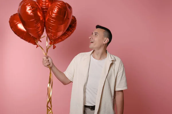 A man is holding red balloons in the shape of a heart on a pink background. Valentine\'s Day, love, February 14. Looks at the balloons