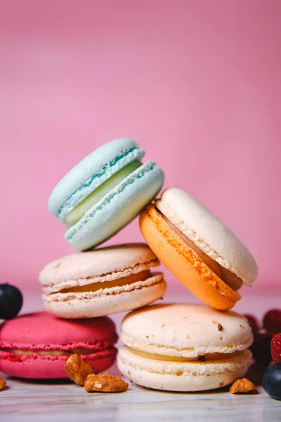 Colorful macarons. Small French cakes. Sweet and colorful french macaroons. Many tasty macarons with fresh berries, raspberries and blueberries, nuts and strawberries on a pink background