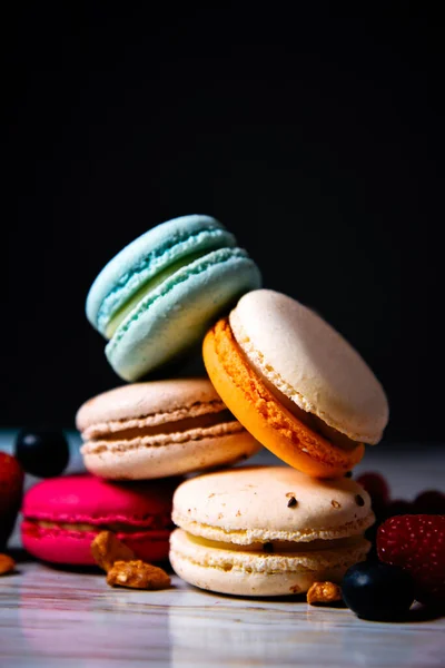 Colorful macarons cakes. Small French cakes. Sweet and colorful french macaroons. Many tasty macarons with fresh berries raspberries and blueberries, nuts on a black background