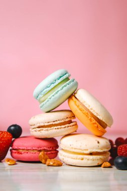 Colorful macarons. Small French cakes. Sweet and colorful french macaroons. Many tasty macarons with fresh berries, raspberries and blueberries, nuts and strawberries on a pink background