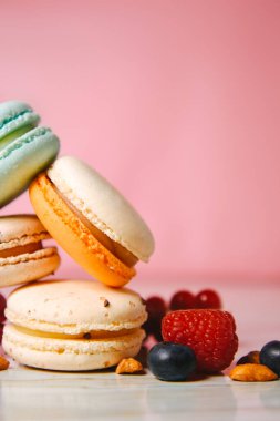 Colorful macarons. Small French cakes. Sweet and colorful french macaroons. Many tasty macarons with fresh berries, raspberries and blueberries, nuts and strawberries on a pink background