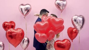 Sevgililer Günü 'nde güzel bir çift 14 Şubat' ı kutluyor, aşkım. Balonların arkasında öpüşen kadın ve erkek kırmızı kalpler, romantik randevu, sarılma, tatlı