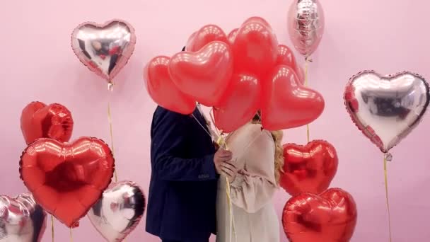 情人节这对年轻漂亮的夫妇庆祝2月14日 男人和女人在气球后面亲吻红心 浪漫的约会 — 图库视频影像