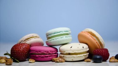 Renkli kurabiyeler. Küçük Fransız kekleri. Tatlı, taze böğürtlenli, ahududulu ve yaban mersinli, fındıklı ve çilekli bir sürü lezzetli badem kurabiyesi mavi arka planda. Karanlıktan aydınlığa geçiş.