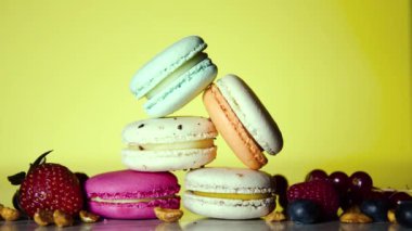 Colorful macarons. Small French cakes. Sweet and colorful french macaroons. Many tasty macarons with fresh berries, raspberries and blueberries, nuts and strawberries on a yellow background