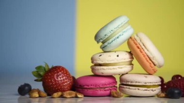 Colorful macarons. Small French cakes. Sweet and colorful french macaroons. Many tasty macarons with fresh berries, raspberries and blueberries, nuts and strawberries on a yellow background
