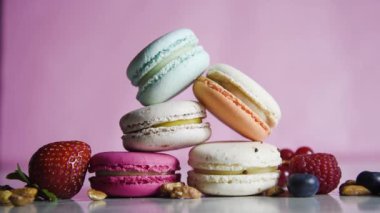 Renkli kurabiyeler. Küçük Fransız kekleri. Tatlı, taze böğürtlenli, ahududulu, yaban mersinli, fındıklı ve çilekli bir sürü lezzetli badem kurabiyesi pembe arka planda. Karanlıktan aydınlığa geçiş.