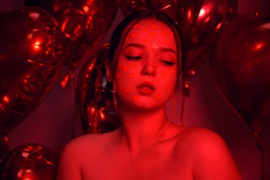 Göğsünde kalp etiketi olan kırmızı neonlu bir kadın kalp şeklinde balonlar taşıyor. Sevgililer Günü için şık bir fotoğraf, aşkım, 8 Mart.