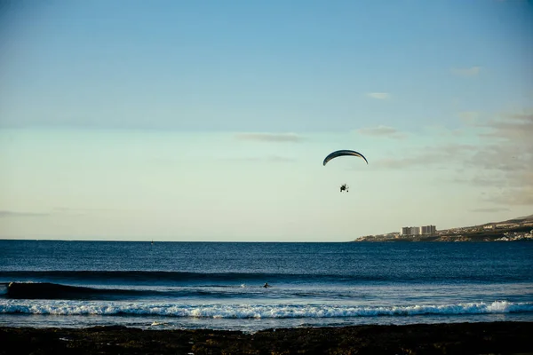 A motorized paraglider flies over the sea, the ocean. Beach recreation. Summer and hobbies.