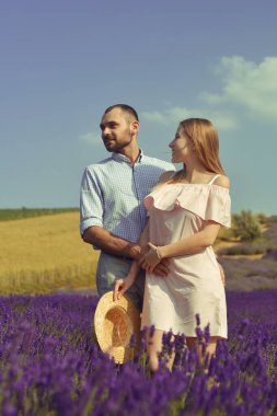 A couple in love in a field of lavender at sunset in good weather. Beautiful woman in a dress and straw panama with a man on the background of nature, love and feelings. Blue, purple lavender