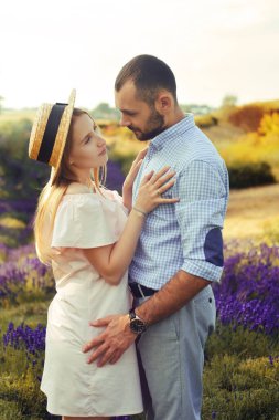 A couple in love in a field of lavender at sunset in good weather. Beautiful woman in a dress and straw panama with a man on the background of nature, love and feelings. Blue, purple lavender