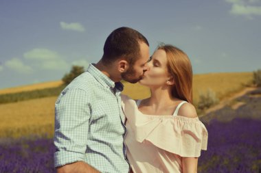 A couple in love in a field of lavender at sunset in good weather. Beautiful woman in a dress and straw panama with a man on the background of nature, love and feelings. Blue, purple lavender